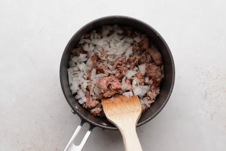 Brown the sausage in a saucepan over medium-high heat, breaking it into pieces.