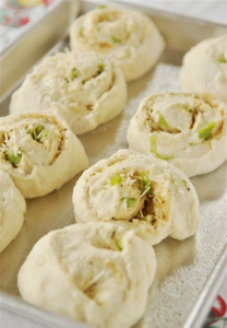 I roll it up into a log, seam side down, and slice it into eight pieces. Those go onto a greased baking sheet. They rise again for about 15 minutes while I finally preheat the oven to 400 degrees.