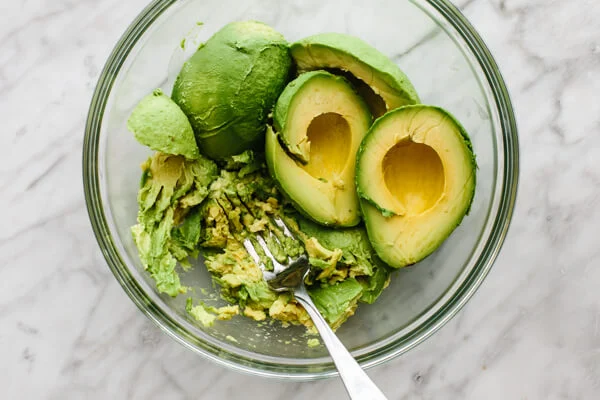 Slice the avocados in half, remove the pits, and scoop the flesh into a mixing bowl