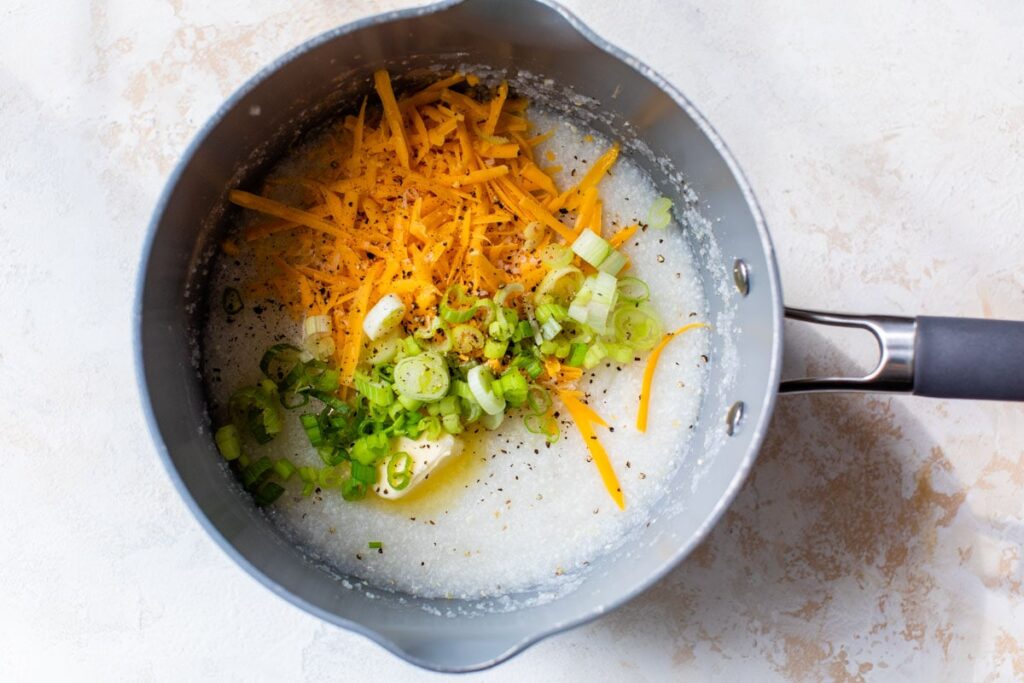 Take the grits off the heat and mix in the butter, black pepper, cheddar, Parmesan, and green onions until creamy