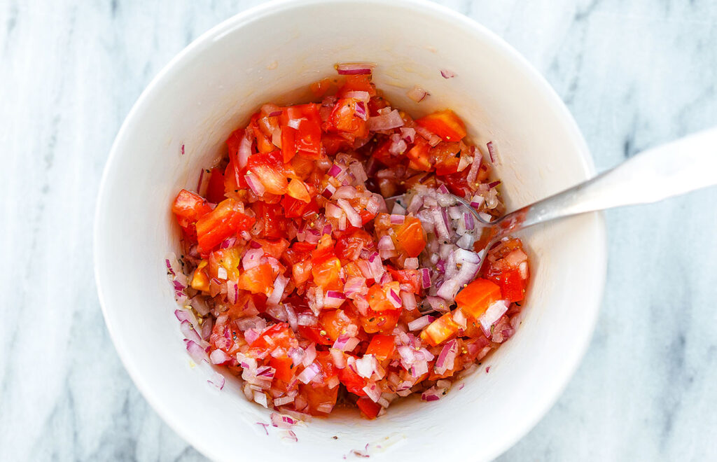 In a bowl, combine the chopped red onion and tomatoes with a few drops of lime juice to create the salsa