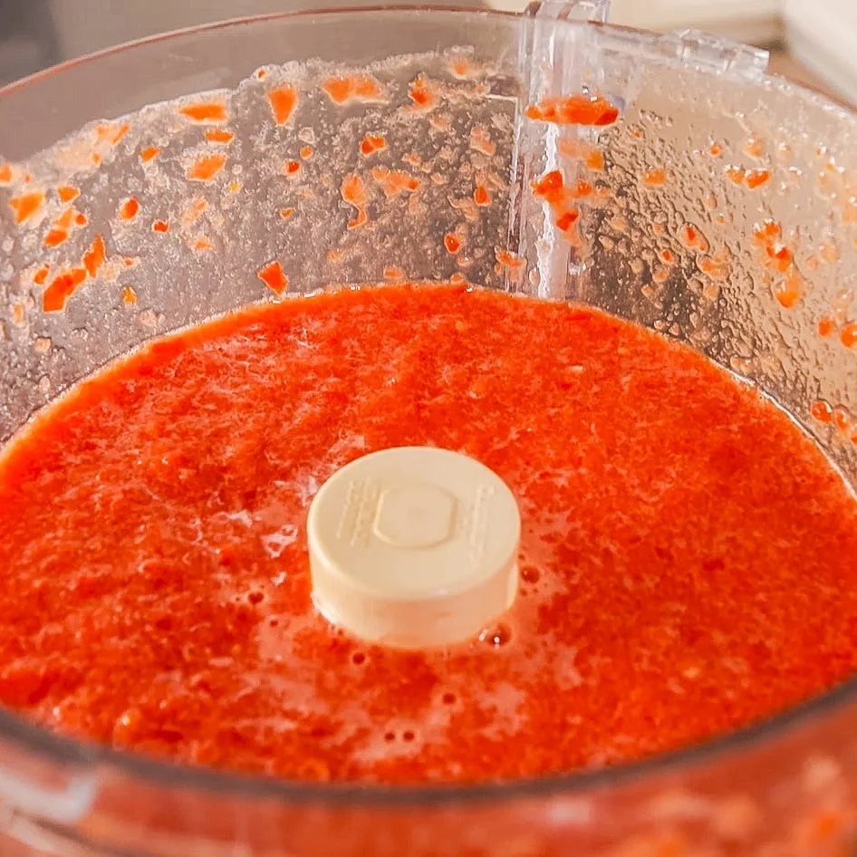In a blender, combine the tomatoes, Scotch bonnet pepper, chopped onion, and bell peppers. Blend until smooth.