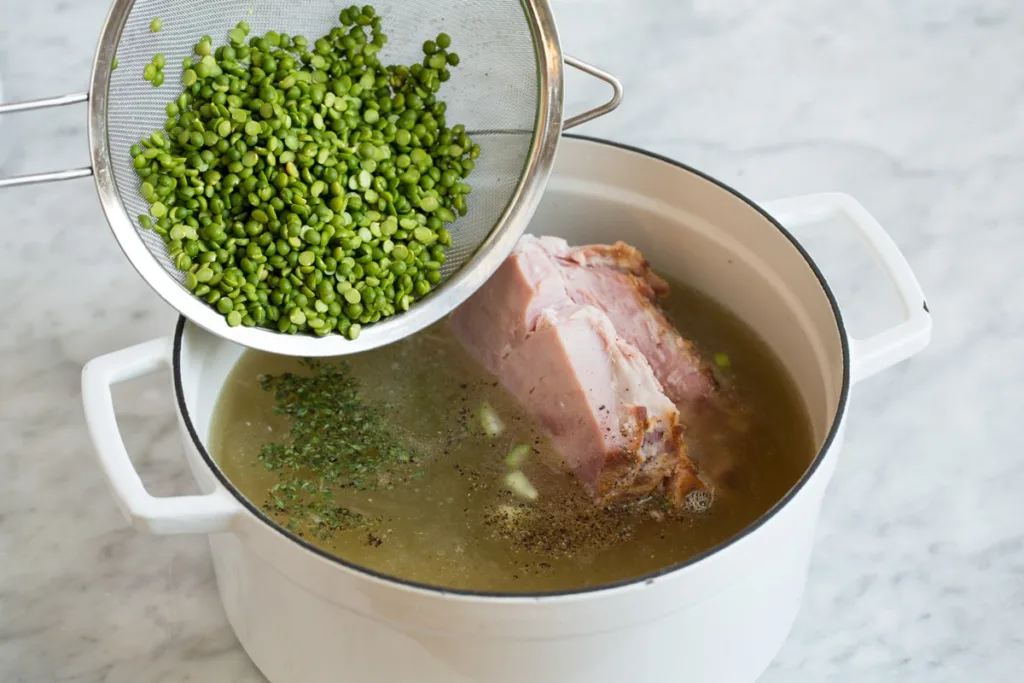 Pour in the chicken broth and water. Add the split peas, bay leaves, and thyme. Season lightly with salt and pepper.