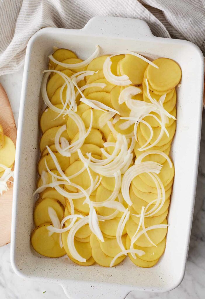 Arrange a layer of sliced potatoes in the bottom of the baking dish, followed by a layer of onions, a portion of the sauce, and a sprinkle of cheese