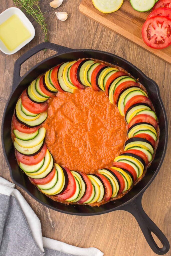 Arrange the sliced eggplant, tomatoes, zucchini, and squash in an overlapping spiral pattern on top of the sauce