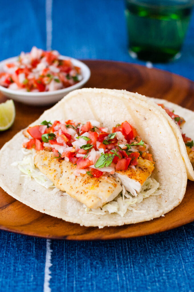 Assemble by placing flaked fish onto each tortilla, topping with salsa, and finishing with a drizzle of spicy sauce