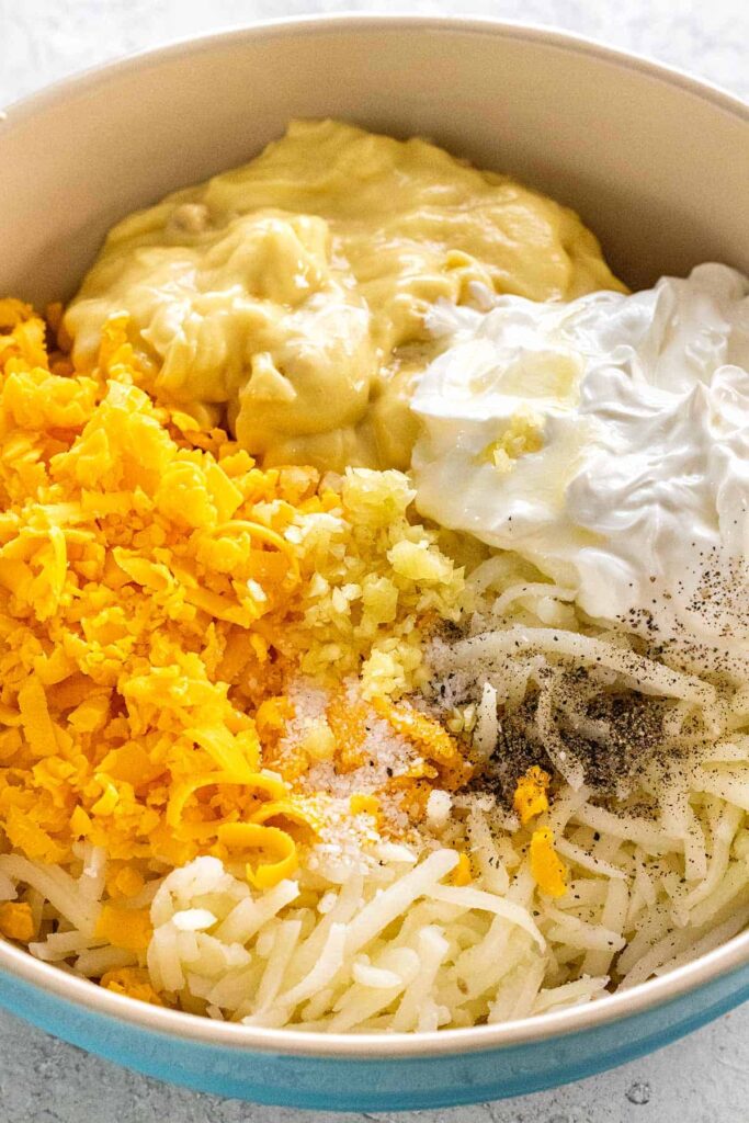 Combine the hashbrowns, part of the shredded cheese, cream of chicken soup, sour cream, onion, melted butter, garlic, salt, and pepper in a large bowl, mixing until everything is evenly incorporated