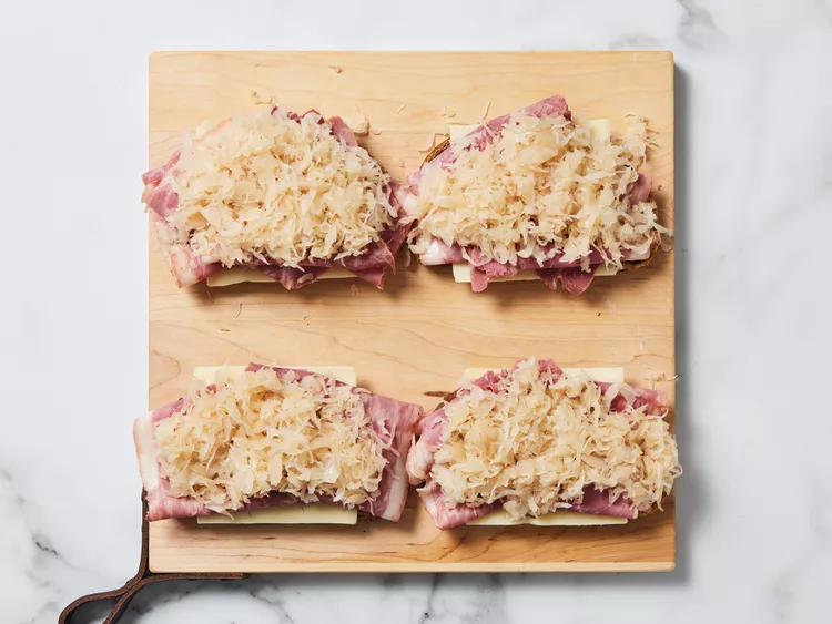 On half of the bread slices, layer a slice of Swiss cheese, corned beef, a portion of drained sauerkraut, and another slice of Swiss cheese