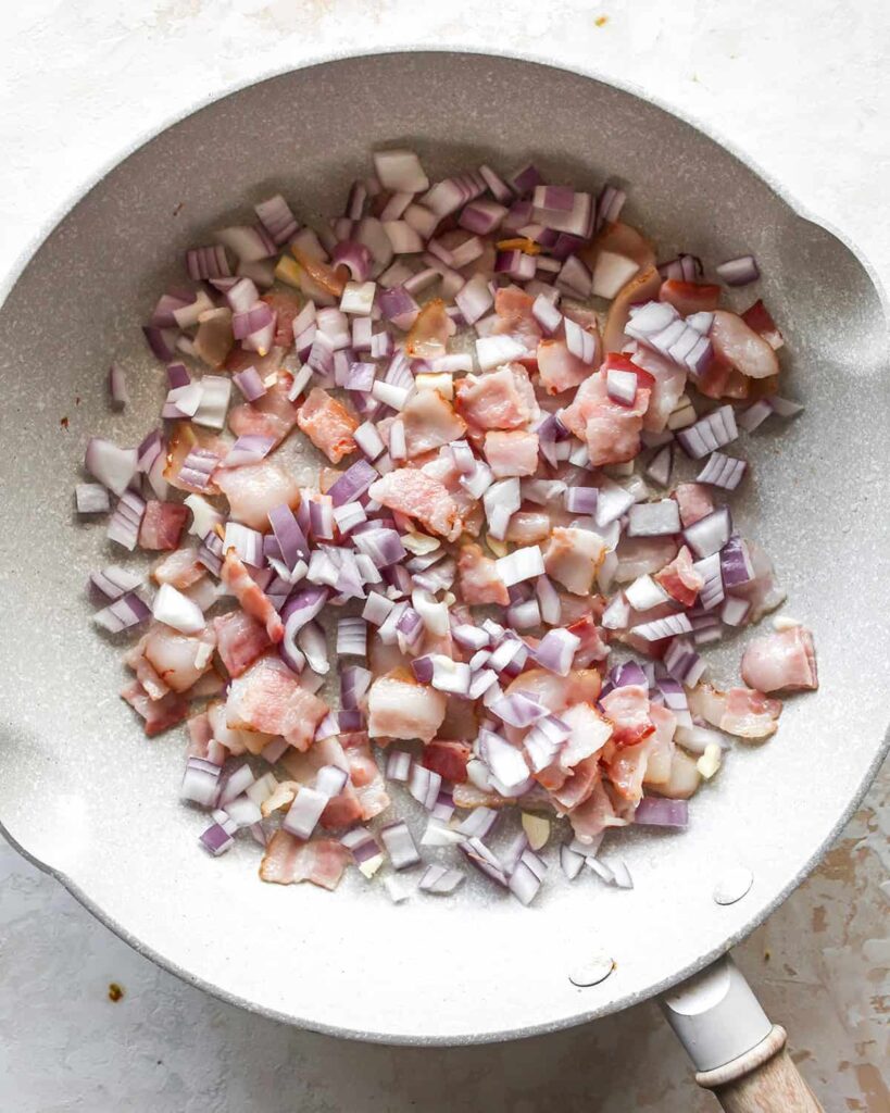 Place the diced bacon in a skillet over medium heat and cook until it begins to soften. Add the chopped onion and minced garlic.