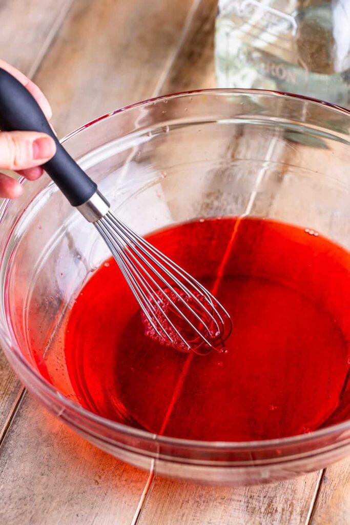 Place the strawberry gelatin mix in a large bowl and pour the boiling water over it. Whisk continuously until the powder is completely dissolved and the liquid appears clear and smooth