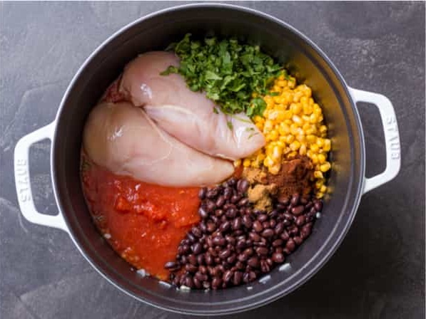 Pour in the chicken broth and crushed tomatoes, then add the chicken breasts, corn, black beans, chili powder, cumin, and salt