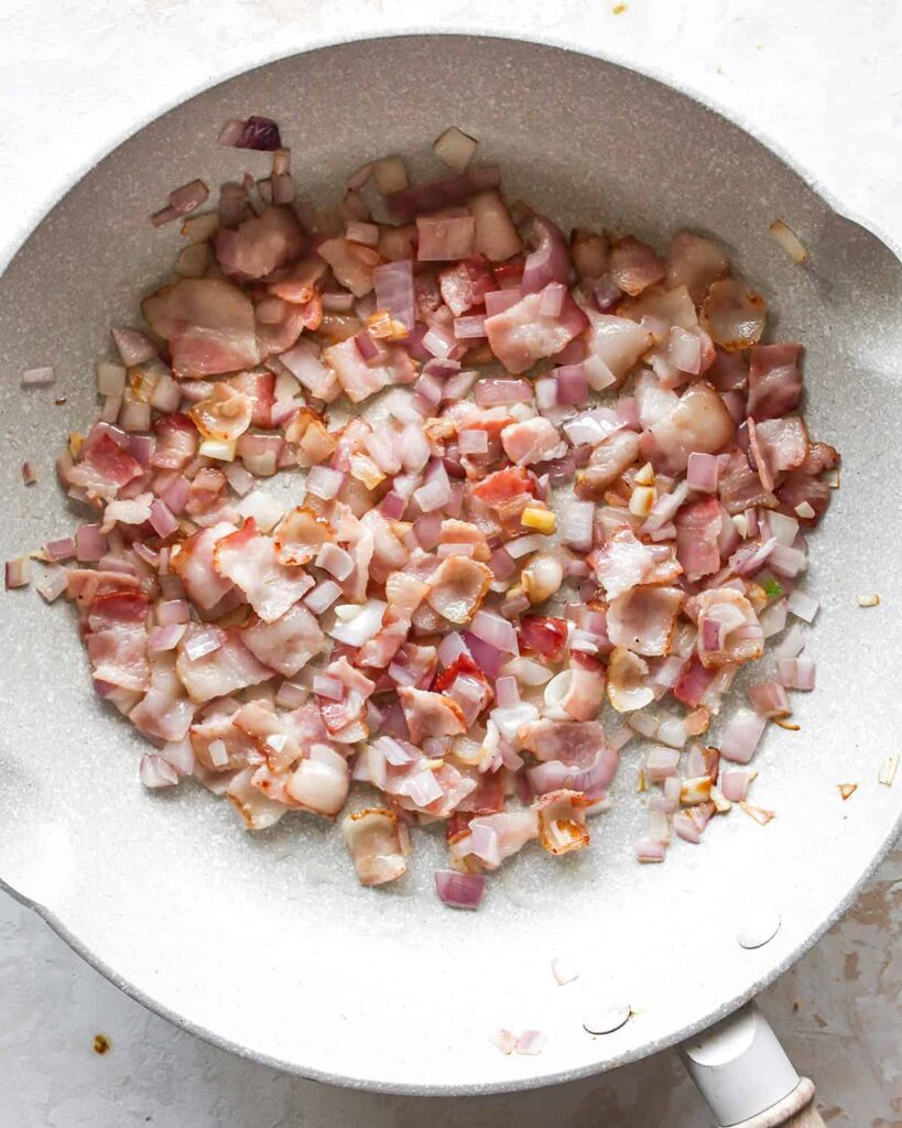 continuing to cook until the bacon starts to brown and the onion becomes tender