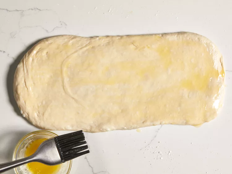 Start by lightly greasing two round cake pans with butter and setting them aside. Roll the thawed bread dough into a rectangle of even thickness on a lightly floured surface. Brush the surface generously with melted butter so the filling sticks well.