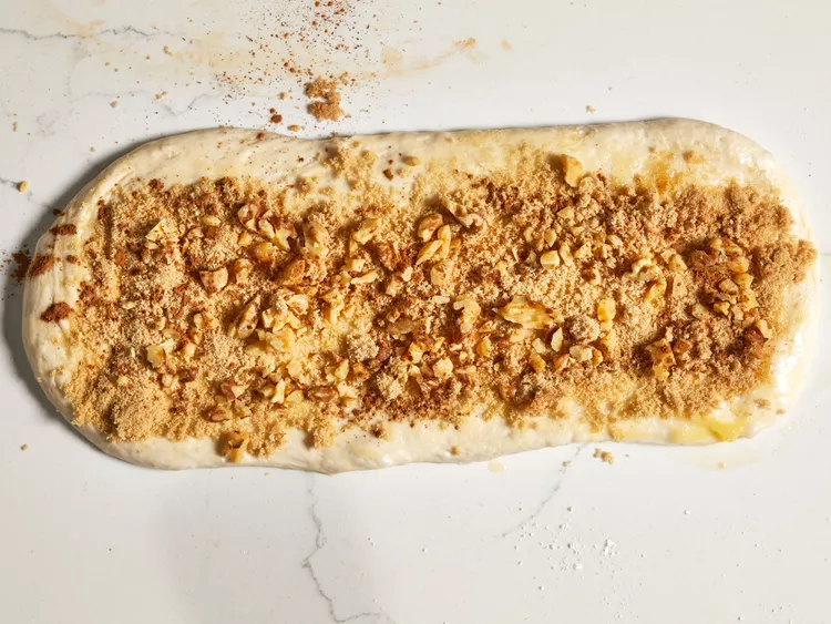 In a small bowl, combine the brown sugar, chopped walnuts, and cinnamon. Sprinkle this mixture evenly over the buttered dough, making sure to cover it from edge to edge. Roll the dough tightly into a log starting from the long side, then lightly moisten the edge with water and seal it closed.