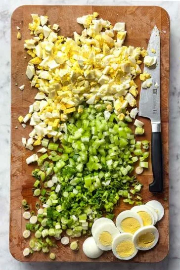 Add the diced celery and green onions to the bowl. Chop most of the hard-boiled eggs and mix them in with the potatoes, reserving one egg for garnish