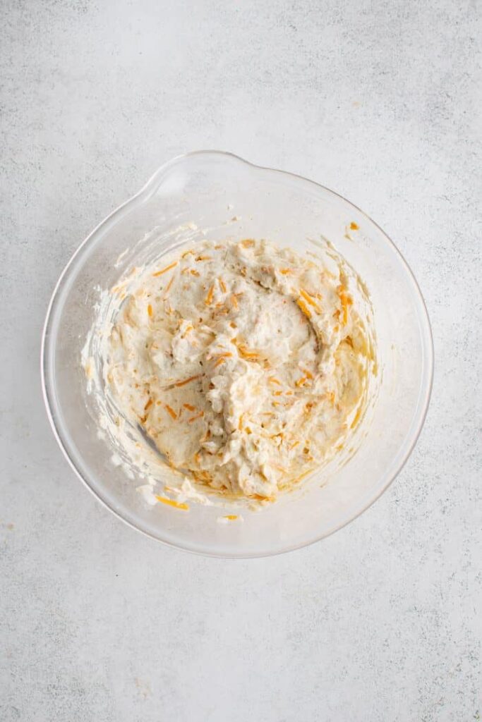 In a large bowl, stir together the shredded cheese, sour cream, cream of chicken soup, half of the melted butter, diced onion, garlic salt, onion powder, and black pepper until well combined 2