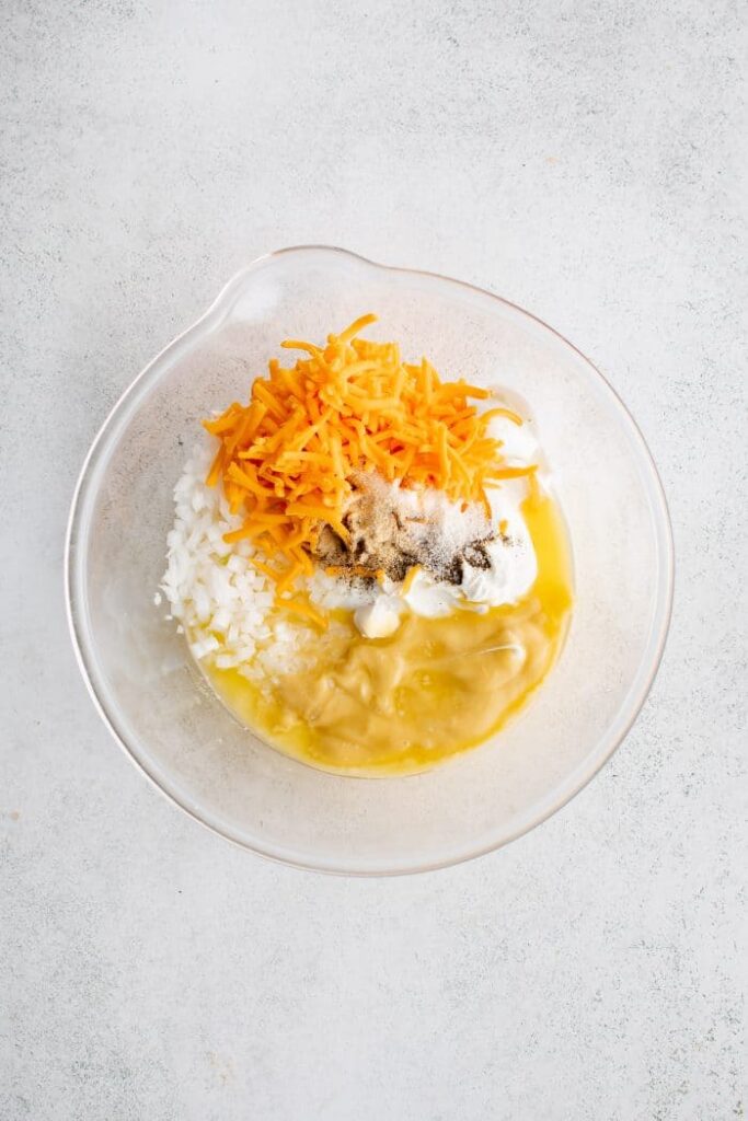 In a large bowl, stir together the shredded cheese, sour cream, cream of chicken soup, half of the melted butter, diced onion, garlic salt, onion powder, and black pepper until well combined