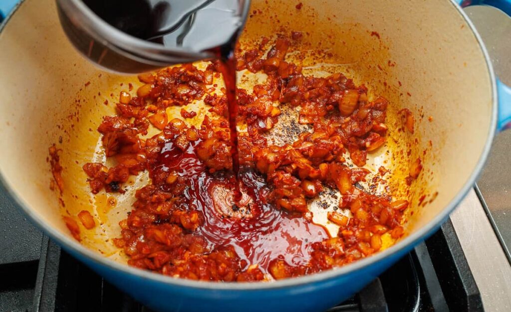Pour in the red wine and scrape the bottom of the pot to release any browned bits. Let it simmer until slightly reduced.