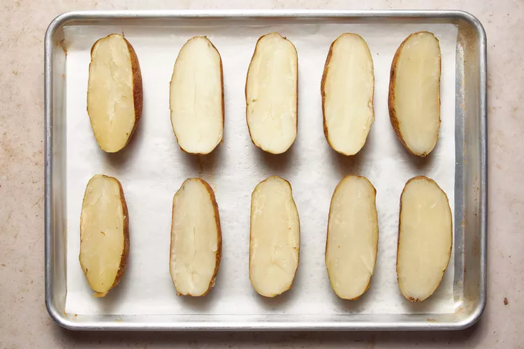 Once the potatoes are done, allow them to cool slightly before cutting them in half lengthwise. Carefully scoop out the insides into a large bowl, leaving a thin layer inside the skins to keep their shape.