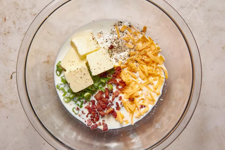 Add sour cream, milk, butter, salt, pepper, half the cheese, half the green onions, and the cooked bacon to the bowl. Mash everything together until creamy and well combined, adjusting the consistency with a little milk if needed.