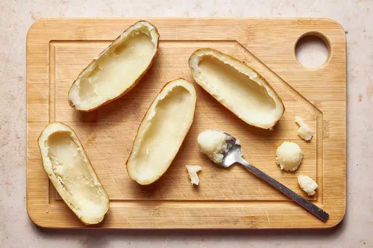 Once the potatoes are done, allow them to cool slightly before cutting them in half lengthwise. Carefully scoop out the insides into a large bowl, leaving a thin layer inside the skins to keep their shape.