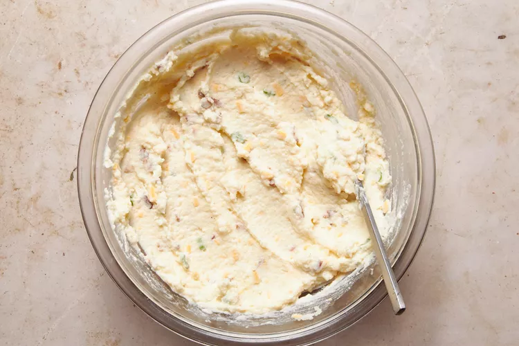 Add sour cream, milk, butter, salt, pepper, half the cheese, half the green onions, and the cooked bacon to the bowl. Mash everything together until creamy and well combined, adjusting the consistency with a little milk if needed.