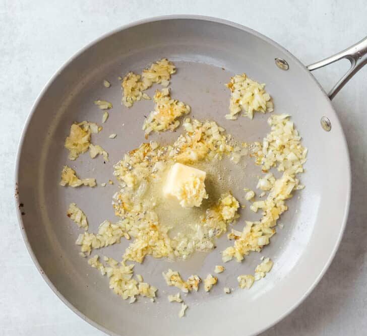 In the same skillet, sauté the diced onion until it starts to soften. Add garlic and butter, stirring until fragrant and melted.