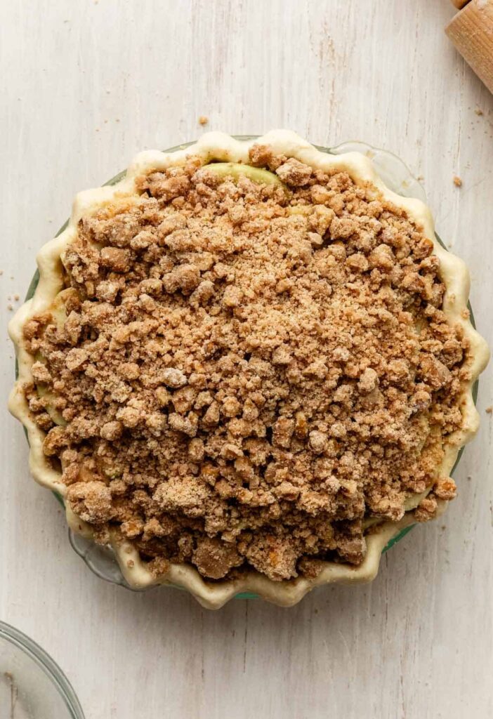 Sprinkle the chilled crumble topping evenly over the apples, covering the entire surface.