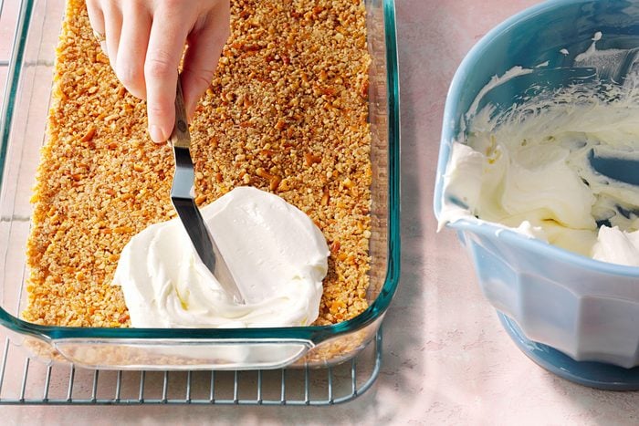 In a separate bowl, beat together the whipped topping, softened cream cheese, and sugar until smooth and creamy. Spread this mixture evenly over the cooled pretzel crust, making sure to seal all edges. Refrigerate until the layer is firm and well chilled.