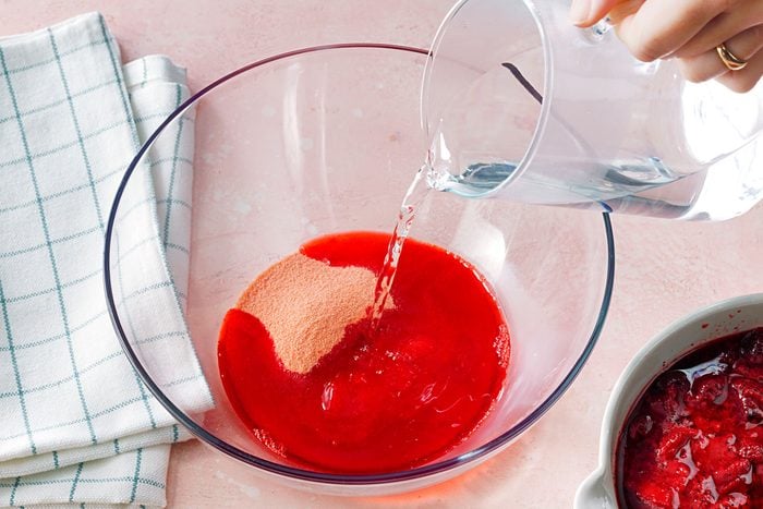 In a large bowl, dissolve the strawberry gelatin in boiling water, stirring until fully dissolved. Add the thawed strawberries and mix well, then refrigerate the mixture until it begins to thicken slightly but is not fully set.