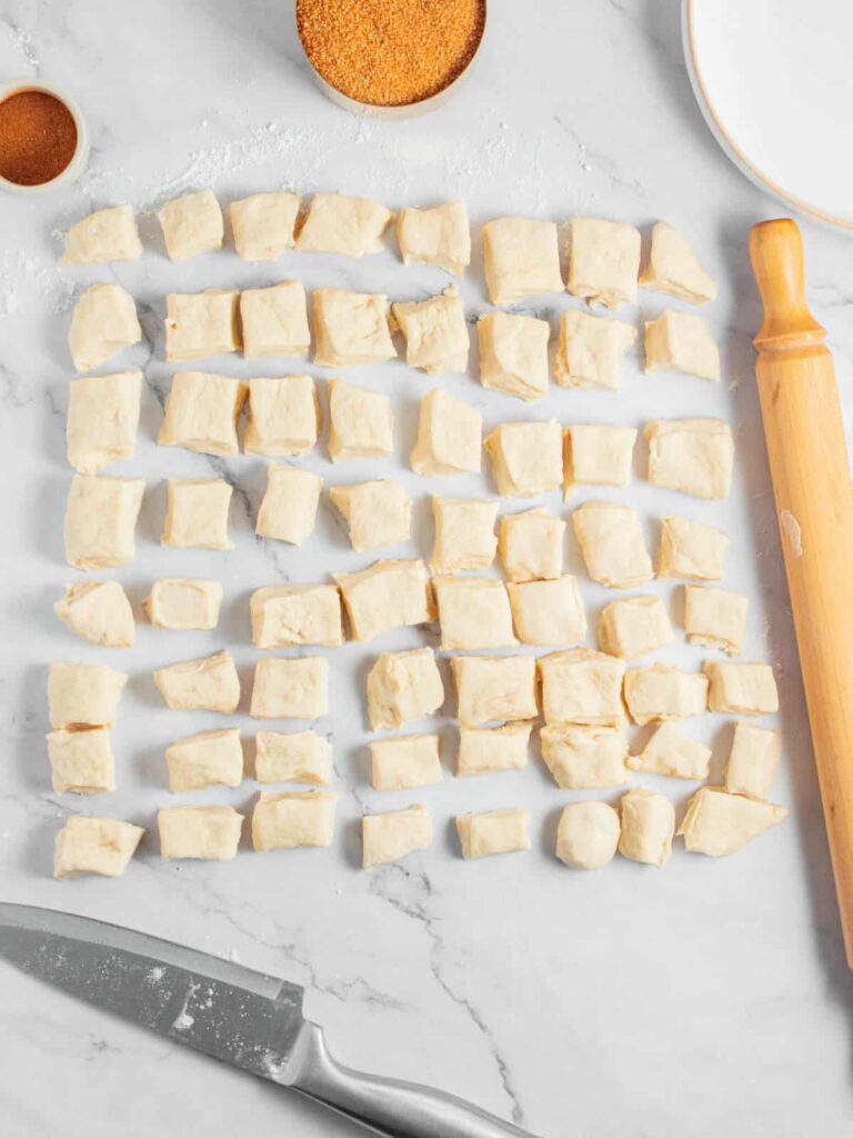 Once risen, gently deflate the dough and move it to a lightly floured surface. Shape it into a rectangle and cut into small pieces, then roll each piece into a ball.
