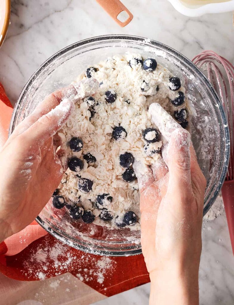Grate the frozen butter directly into the flour mixture using a box grater, then gently toss and work it in with your hands until the texture resembles coarse crumbs. Add the blueberries and mix lightly to distribute them evenly.